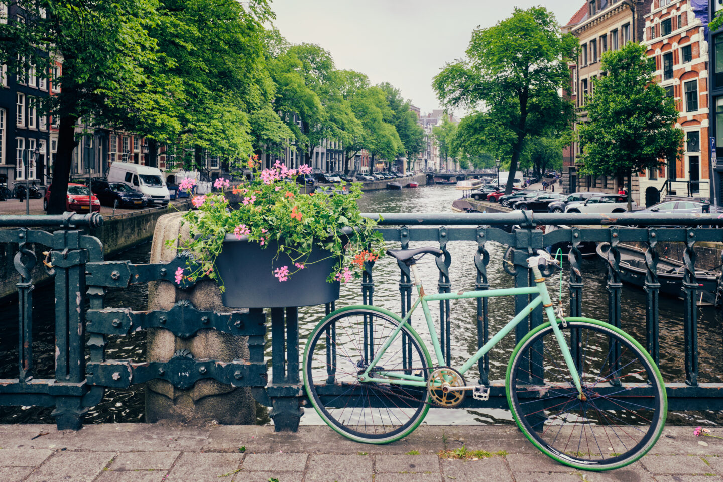 Amsterdam canal with boats and parked bicycles on a bridge with flowers.