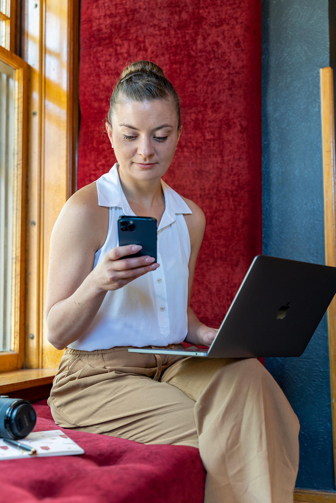 Woman sitting in window with computer in her lap and working on her phone